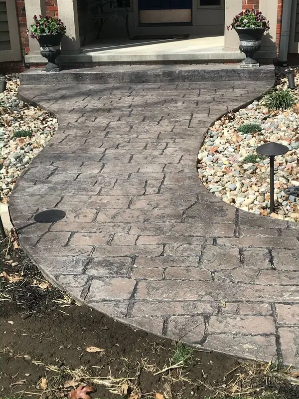 Curved stamped concrete walkway in a cobblestone pattern with a contrasting tooled border running alongside a lawn