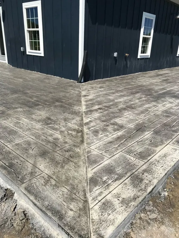 Corner of a wood-plank stamped concrete slab showing the plank end joints and grain texture where two runs meet